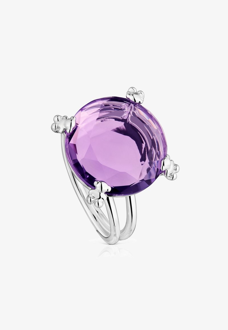 Pierścionek z fioletowym fasetowanym kamieniem szlachetnym osadzonym w trzech srebrnych obrączkach z akcentami w kształcie kwiatów wokół kamienia. Gładka faktura, wypolerowane wykończenie.