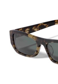 Des lunettes de soleil en écaille de tortue avec des montures épaisses, un design angulaire, des verres gris et une finition brillante. Des accents de motifs beige clair et crème.