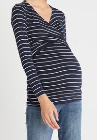 Mörkblå långärmad topp med vita horisontella ränder, med en crossover-design fram, mjukt tyg och en avslappnad passform för gravidkläder.