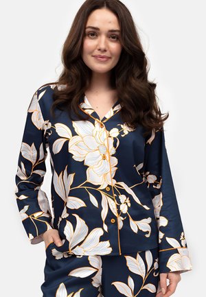 Ensemble de pyjama en satin bleu marine avec un grand imprimé floral blanc et orange, comprenant une chemise à boutons et des manches longues, associé à un pantalon assorti.