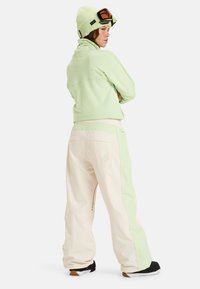 Mintgrön zip-up-jacka med en texturerad mönster, i kombination med krämfärgade avslappnade byxor med mintgröna accenter och sidodragkedjefickor.
