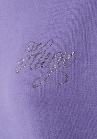 Indumento lavorato a maglia viola con un logo "Hugo" in argento metallico, scritto in un font corsivo. Texture liscia con un design a maglia stretta e dettagli raffinati.