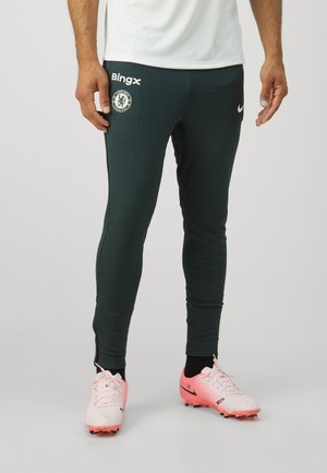 Grønne atletiske bukser med ribbet tekstur, Nike-logo og Chelsea FC-mærke. Har en slim fit og kontrasterende sidelister.