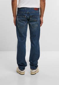 Donkerblauwe denimjeans met een relaxed fit, voorzien van twee achterzakken met gebogen kleppen en een leren patch op de tailleband.