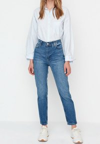 Light blue striped button-up shirt, high-waisted blue denim jeans, and white sneakers. Casual outfit with relaxed fit and cuffed sleeves.