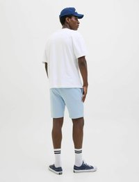 T-shirt blanche à manches courtes associée à un short bleu clair, chaussettes blanches avec des rayures noires et baskets bleu marine. Le modèle est tourné sur le côté.