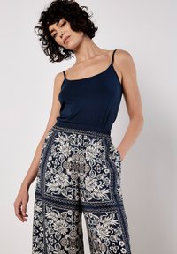 Marineblaues Tanktop mit dünnen Trägern, kombiniert mit weit geschnittenen, gemusterten Hosen mit floralem Design in Creme und Dunkelblau.