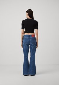 Črn kratki top s kratkimi rokavi v kombinaciji s plavimi širokimi jeans hlačami. Hlače imajo rdečo oznako "HUGO" na zadnjem pasu. Gladka tekstura.