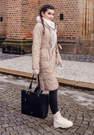 Beige gesteppter Mantel mit gebundenem Taillengürtel, weißem Schal, schwarzer Handtasche mit silbernem Zubehör, dunklen Jeans und weißen Knöchelstiefeln mit Schnürsenkeln.