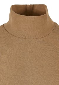 Maglione a collo alto in maglia a coste color beige. La texture è liscia e il tessuto appare morbido, ideale per essere indossato a strati.