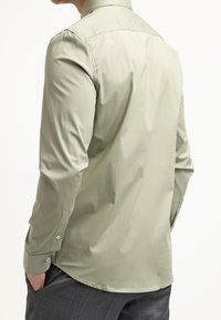 Hellgrünes Langarmhemd aus glattem Stoff, mit einem klassischen Kragen, geknöpften Manschetten und einem abgerundeten Saum hinten.