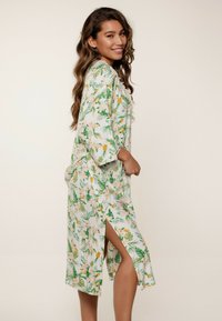 Kimono floral con hojas verdes y flores durazno, que presenta un ajuste relajado, aberturas laterales, mangas hasta el codo y una tela ligera.