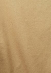 Tissu beige uni avec un subtil motif de tissage diagonal et de légères rides créant des ombres douces.