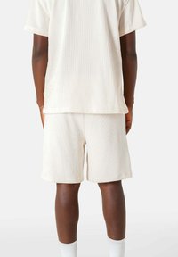 Lichtbeige set bestaande uit een getextureerd, kortmouwtop en shorts met een losse pasvorm, gecombineerd met witte kniehoge sokken.