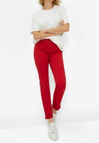 Jeans in denim rosso con vestibilità slim, orli arrotolati, abbinati a una maglietta bianca ampia e sneaker bianche. Tessuto liscio, design casual.