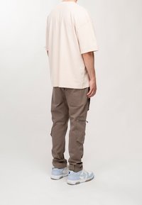Beige Baumwoll-Übergrößen-T-Shirt, braune Cargo-Hosen mit seitlichen Reißverschlüssen und hellblaue Sneakers. Einfaches Design, lockere Passform und weiche Textur.