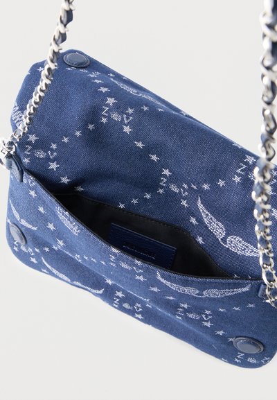 Sac d'épaule en tissu bleu avec motifs d'étoile blanche et d'ailes, bandoulière en chaîne argentée, et fermeture à bouton-pression, présenté ouvert vu de dessus.