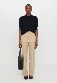 Polo shirt navy cu mânecă scurtă, asortat cu pantaloni drepti bej. Modelul ține o geantă neagră cu formă rotundă, completată de pantofi negri joși.