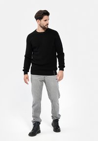 Schwarzer gestrickter Pullover mit rundem Halsausschnitt und langen Ärmeln, kombiniert mit hellgrauen Jeans und schwarzen Schnürstiefeln. Minimalistisches Design.
