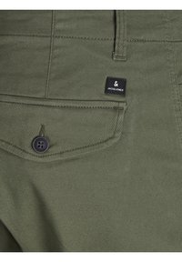 Gros plan d'une poche de pantalon vert olive avec un bouton noir et une petite étiquette noire indiquant la marque Jack & Jones.