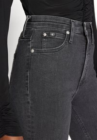 High-rise black denim jeans with a slim fit, contrast stitching, front pocket detailing, and a CK logo tab on the waistband.
