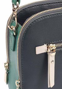 Sac en cuir noir porté croisé avec une accentuation verte. Il dispose de zips dorés et de quincaillerie, ainsi qu'une finition texturée. Tirettes de fermeture éclair notables en blanc.