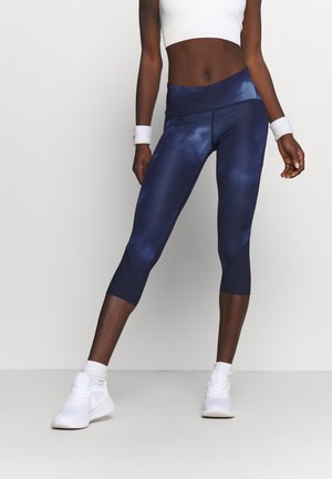 Leggings capri bleu marine en matériau texturé et respirant. Présentent une taille haute et des accents de design angulaires. Portés avec des baskets blanches.