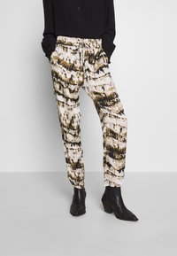 Pantaloni a gamba ampia con un motivo tie-dye bianco, marrone e nero. Vita elastica con cordoncino, gamba affusolata e tessuto leggero.