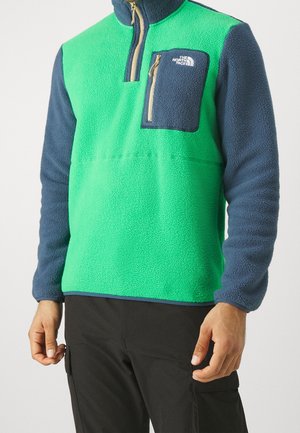 Pull en polaire vert vif et bleu marine, doté d'un col zippé à mi-hauteur, d'une poche sur la poitrine et d'un tissu texturé pour plus de chaleur.