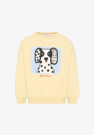 Sweatshirt jaune pâle avec un chien Dalmatien en dessin animé, aux oreilles de motifs différents, avec le texte "Bobo Choses" sous l'image.