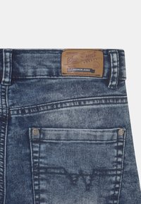 Donkerblauwe denim jeans met een vervaagde afwerking, voorzien van een leren label met de tekst "Blue Effect" en decoratieve stiksels op de achterzakken.