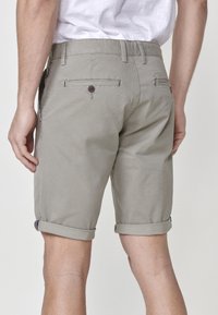 Pantaloni scurți gri din bumbac cu tiv rulat, două buzunare la spate cu închidere cu buton și un finisaj texturat. Accente de cusături detaliate.