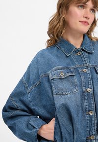 Leren spijkerjas in lichtblauw, met een knoopsluiting aan de voorkant, twee borstzakken en een kraag. Zachte textuur met een ontspannen pasvorm.