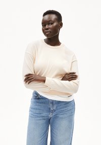  lichtroze lange mouw trui met een ronde hals, geribbelde manchetten en zoom, gecombineerd met blauwe denim jeans met een klassieke pasvorm en naden.