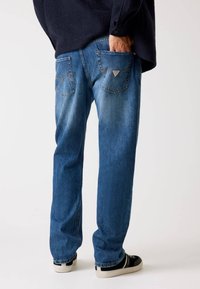 Blaue Jeans mit geradem Schnitt, ausgestattet mit zwei Gesäßtaschen und subtiler Waschung. Kombiniert mit schwarzen Sneakers für einen lässigen Look.