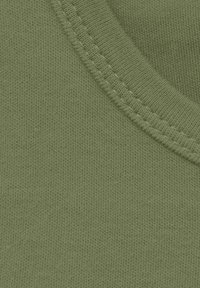 Tela de algodón verde con una textura suave, que presenta un escote acanalado y detalles de costura visibles a lo largo de los bordes.