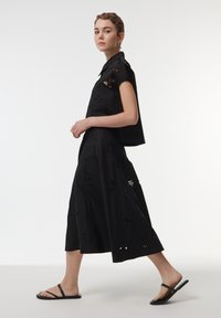Top corto negro con mangas cortas y bordado floral, combinado con una falda negra hasta la rodilla con recortes y un acabado texturizado. Sandalias negras.