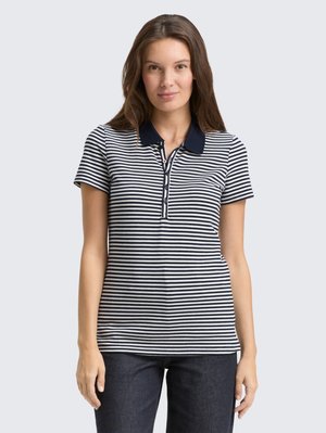 Polo rayé bleu marine et blanc avec un col, des manches courtes et une patte de boutonnage. Fabriqué en tissu doux, porté avec un jean noir.