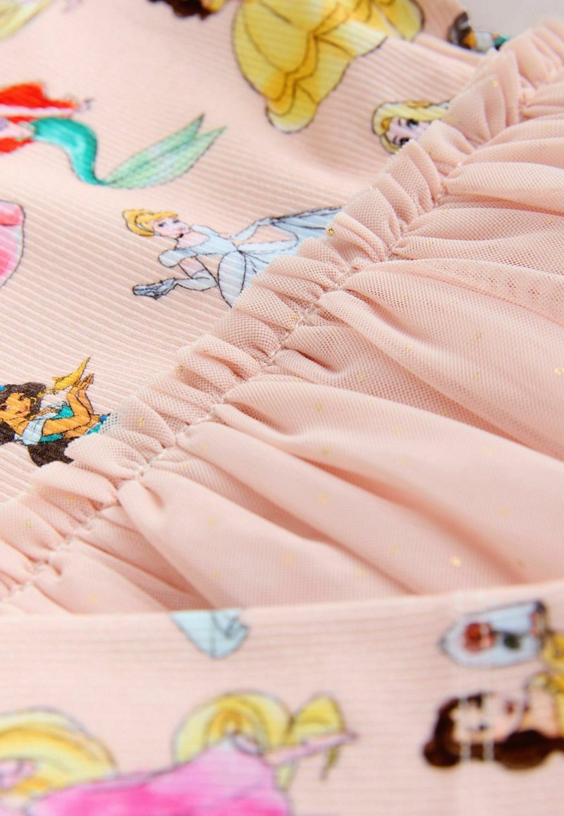 Tissu rose pâle avec des princesses de dessin animé imprimées et une surcouche de tulle froncé, décorée de doux pois dorés.