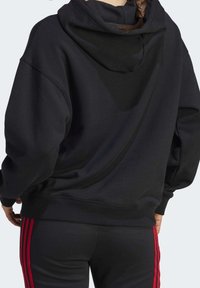 Sweat-shirt à capuche noir avec une coupe décontractée et des poignets côtelés. Présente une texture lisse et des lignes de design subtiles au dos.