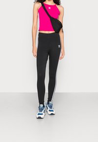 Åtsittande rosa crop top, svarta högmidjade leggings med vita sidostrickor, och blå och vita träningsskor. Svart axelväska.