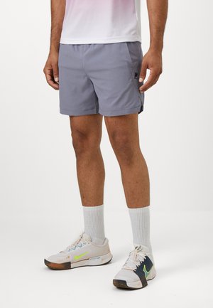 Pantalones cortos deportivos grises con un diseño sencillo, cortes laterales y un logo en la pierna izquierda. Combínalos con calcetines blancos y zapatillas con detalles en verde.
