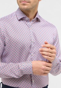 Weißes Hemd mit Knopfleiste und geometrischem Muster aus roten und blauen Quadraten. Mit einem Kentkragen und Knopfmanschetten, gefertigt aus leichtem Stoff.