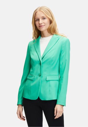 Grün satinierter Blazer mit Reverskragen, zwei vorderen Taschen und taillierter Silhouette. Mit Knöpfen zum Schließen, kombiniert mit einem schwarzen Unterteil.