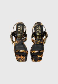 Sandálias de salto alto pretas com padrão floral dourado, biqueira quadrada e tiras para o tornozelo. Apresenta uma palmilha com marca e detalhes decorativos de fivela.