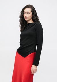 Μαύρο τοπ με μακριά μανίκια, λαιμόκοψη bateau και καμπύλη λαιμόκοψη, συνδυασμένο με κόκκινη σατέν φούστα με ομαλή υφή και γυαλιστερό φινίρισμα.