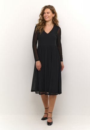Zwarte jurk met lange doorzichtige mouwen, V-hals en ingezette taille. De rok is knielang met een vloeiende, lichte textuur.