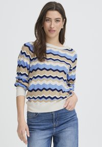 Pull multicolore présentant un motif en zigzag bleu, beige et marine, avec poignets et ourlet côtelés. Tissu tricot léger avec une coupe décontractée.