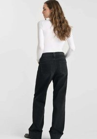 Zwarte hoogangered spijkerbroek in denim stof, met een recht model, twee achterzakken en opgerolde boorden. Draagt met een wit top.