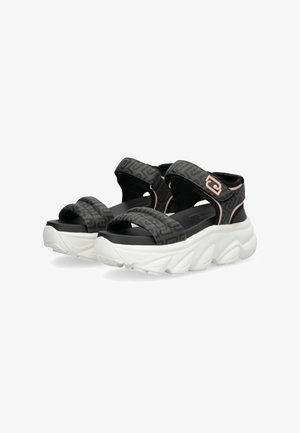 Sandales noires à motifs avec deux brides ajustables et une semelle épaisse blanche. Elles présentent une tige texturée et un design à bout arrondi.